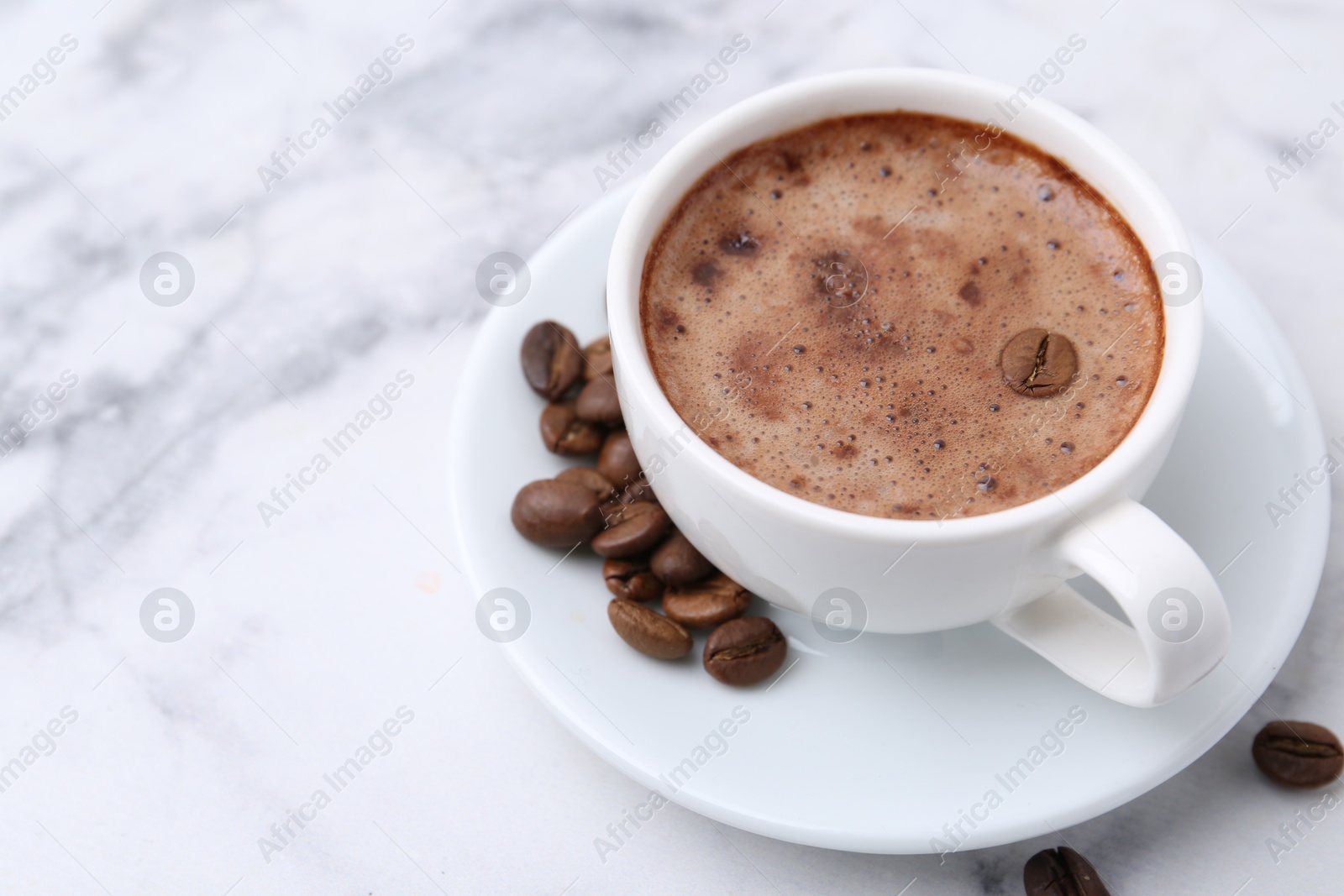 Aromatic coffee in cup, beans and saucer on white marble table, closeup. Space for text Photo of Aromatic coffee in cup, beans and saucer on white marble table, closeup. Space for text