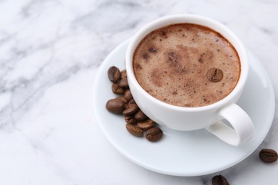 Photo of Aromatic coffee in cup, beans and saucer on white marble table, closeup. Space for text