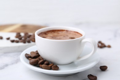 Photo of Aromatic coffee in cup, beans and saucer on white marble table, closeup