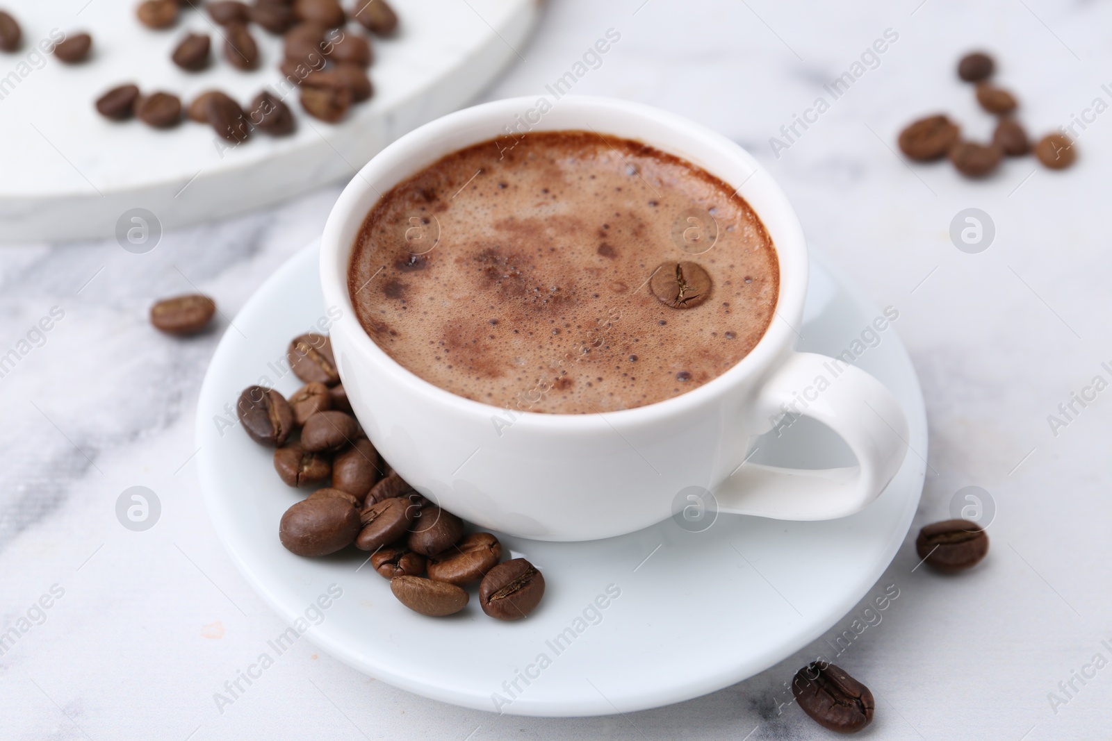 Aromatic coffee in cup, beans and saucer on white marble table, closeup Photo of Aromatic coffee in cup, beans and saucer on white marble table, closeup