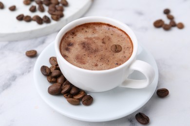 Photo of Aromatic coffee in cup, beans and saucer on white marble table, closeup