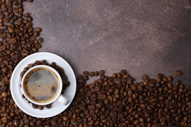 Photo of Aromatic coffee in cup, saucer and beans on brown textured table, flat lay. Space for text