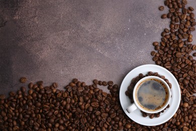 Photo of Aromatic coffee in cup, saucer and beans on brown textured table, flat lay. Space for text