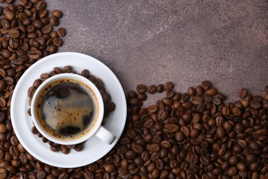 Photo of Aromatic coffee in cup, saucer and beans on brown textured table, flat lay. Space for text