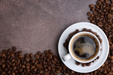 Photo of Aromatic coffee in cup, saucer and beans on brown textured table, flat lay. Space for text