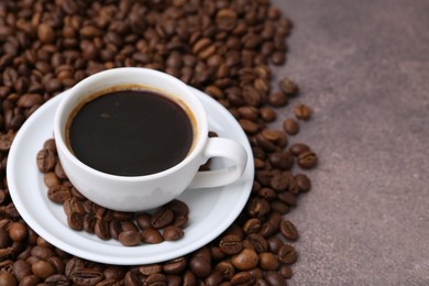 Photo of Aromatic coffee in cup, saucer and beans on brown textured table, closeup. Space for text