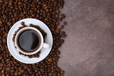 Photo of Aromatic coffee in cup, saucer and beans on brown textured table, flat lay. Space for text