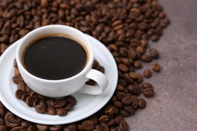 Photo of Aromatic coffee in cup, saucer and beans on brown textured table, closeup