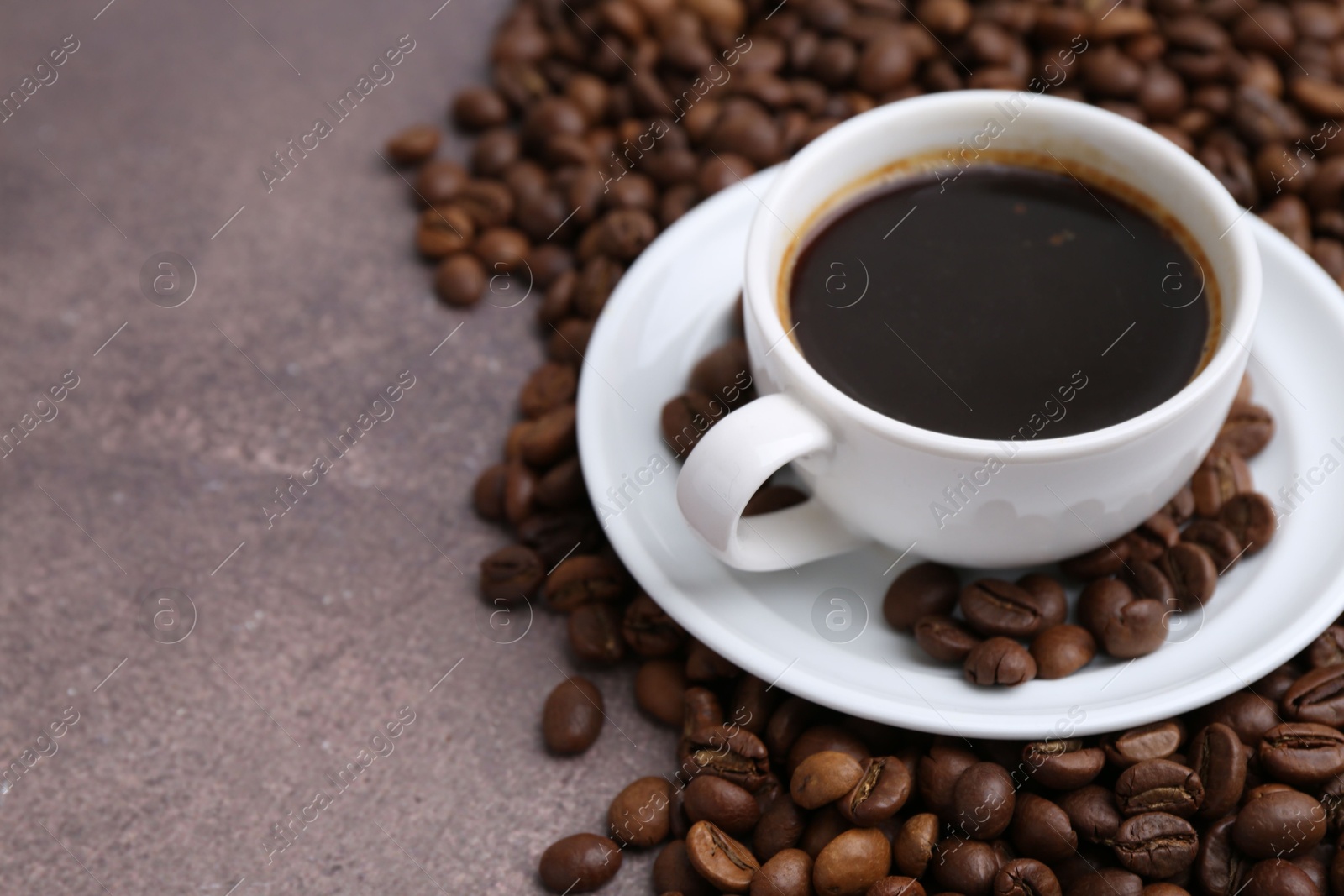 Aromatic coffee in cup, saucer and beans on brown textured table, closeup. Space for text Photo of Aromatic coffee in cup, saucer and beans on brown textured table, closeup. Space for text