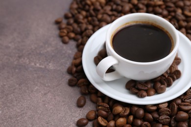 Photo of Aromatic coffee in cup, saucer and beans on brown textured table, closeup. Space for text