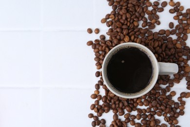 Photo of Aromatic coffee in cup and beans on white tiled table, flat lay. Space for text