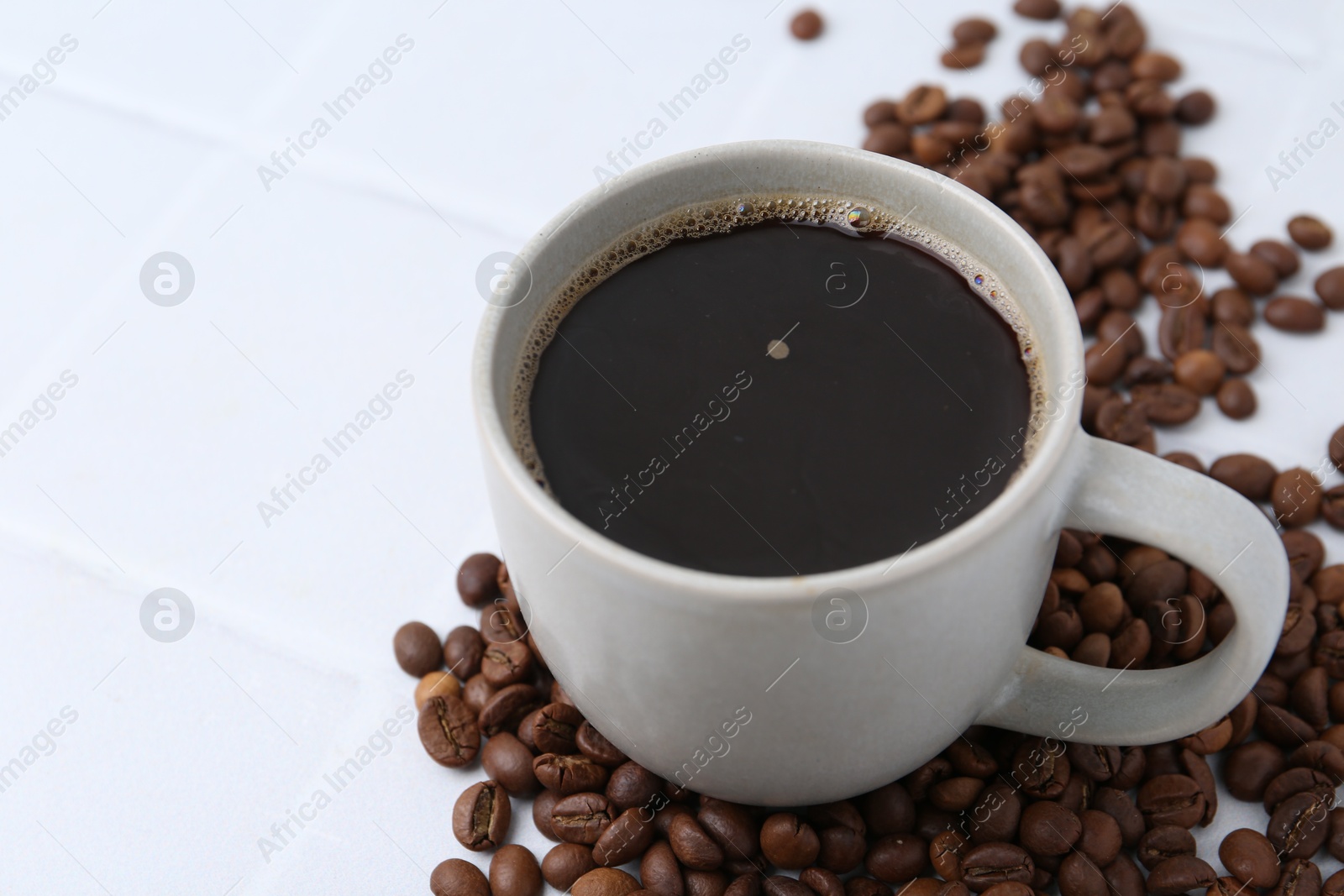Aromatic coffee in cup and beans on white tiled table, closeup. Space for text Photo of Aromatic coffee in cup and beans on white tiled table, closeup. Space for text