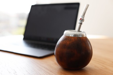 Photo of Traditional yerba mate tea and laptop on wooden table indoors, closeup