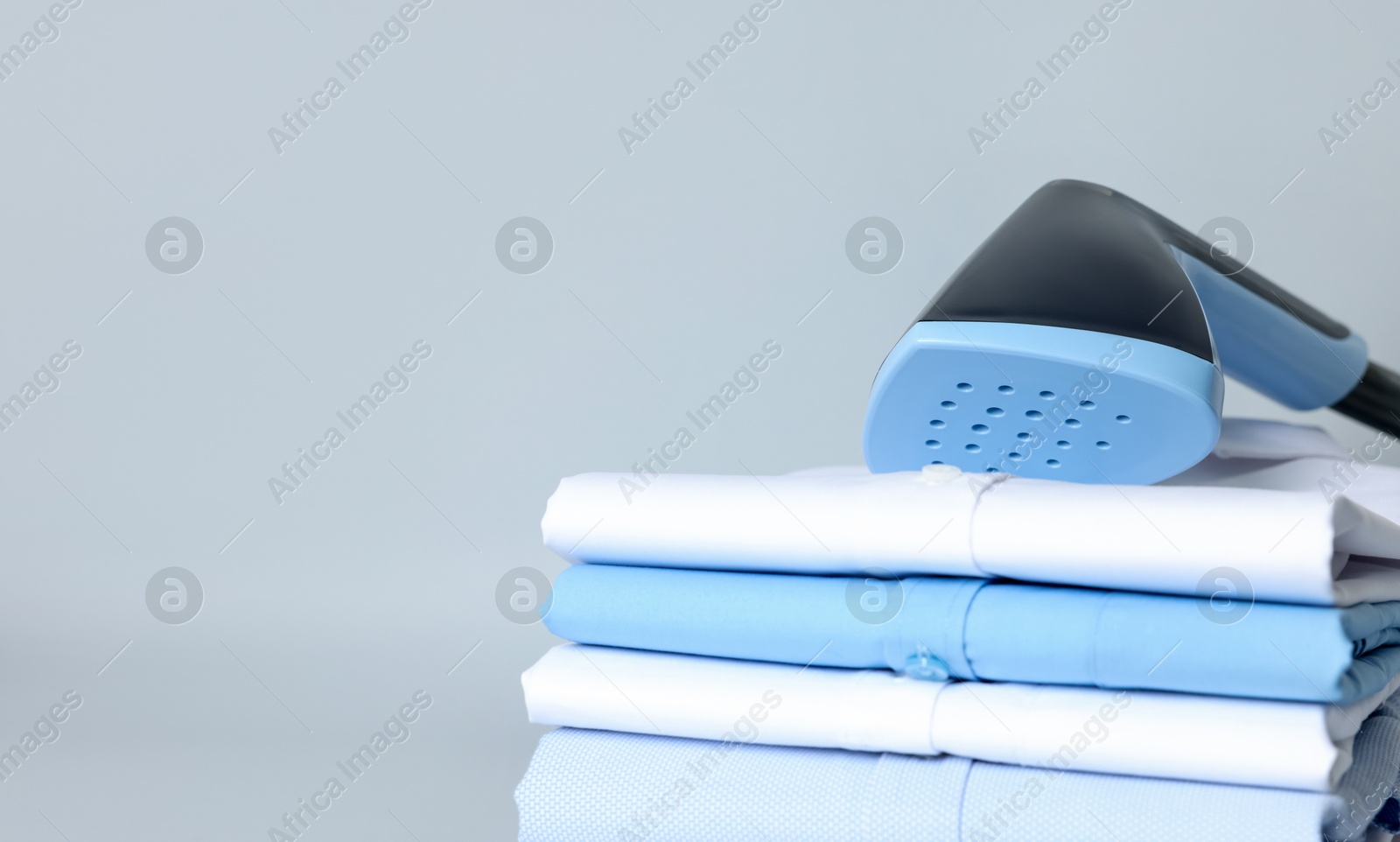 Upright steamer and stack of folded clothes on grey background, closeup. Space for text Photo of Upright steamer and stack of folded clothes on grey background, closeup. Space for text