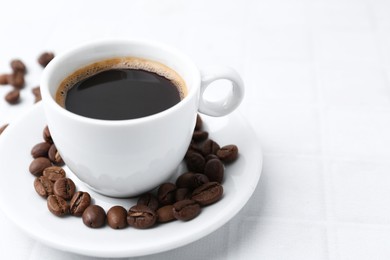 Photo of Aromatic coffee in cup and beans on white table, closeup. Space for text