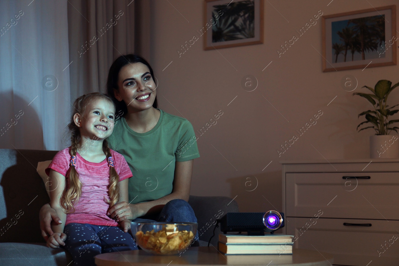 Young woman and her daughter watching movie using video projector at home. Space for text Photo of Young woman and her daughter watching movie using video projector at home. Space for text