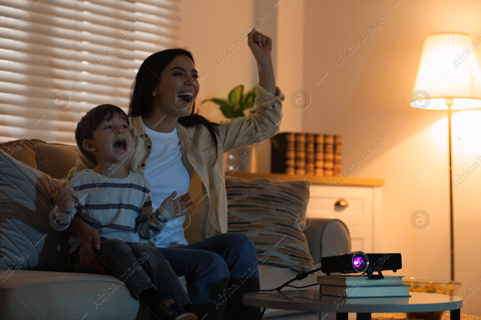 Emotional young woman and her son watching TV using video projector at home. Space for text Photo of Emotional young woman and her son watching TV using video projector at home. Space for text