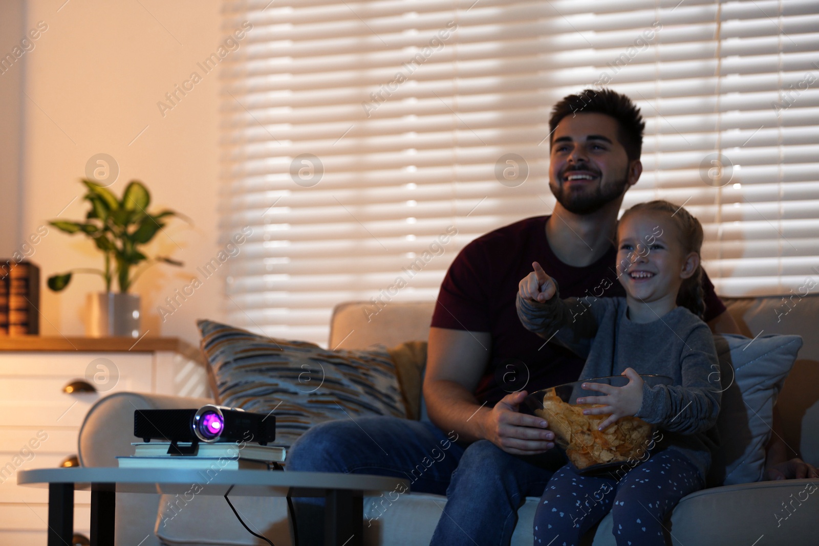 Young man and his daughter watching movie using video projector at home. Space for text Photo of Young man and his daughter watching movie using video projector at home. Space for text