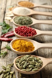 Photo of Different aromatic spices in spoons on wooden table, closeup