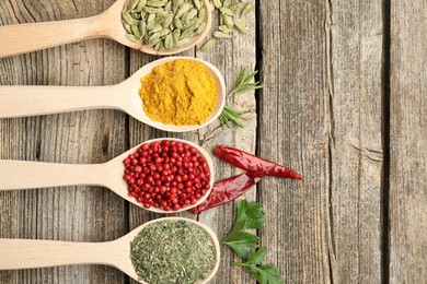 Photo of Different aromatic spices in spoons on wooden table, flat lay. Space for text