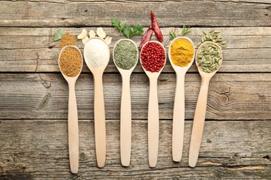 Photo of Different aromatic spices in spoons on wooden table, flat lay