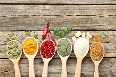 Photo of Different aromatic spices in spoons on wooden table, flat lay. Space for text