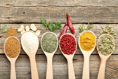 Photo of Different aromatic spices in spoons on wooden table, flat lay