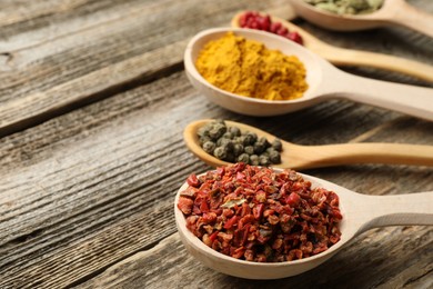 Photo of Different aromatic spices in spoons on wooden table, closeup. Space for text