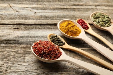 Photo of Different aromatic spices in spoons on wooden table, closeup. Space for text