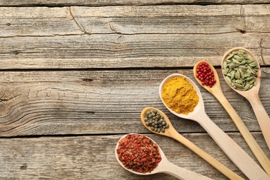 Photo of Different aromatic spices in spoons on wooden table, flat lay. Space for text