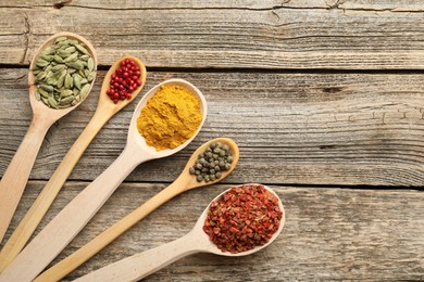 Photo of Different aromatic spices in spoons on wooden table, flat lay. Space for text