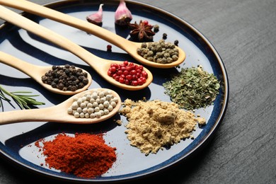 Photo of Different aromatic spices in spoons on black table, closeup