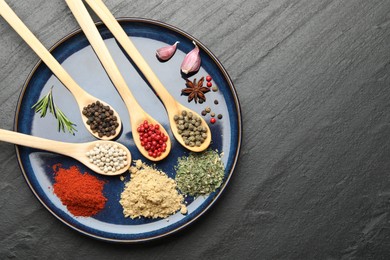 Photo of Different aromatic spices in spoons on black table, top view. Space for text