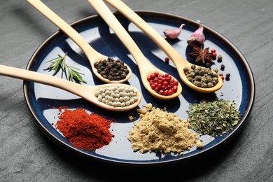 Photo of Different aromatic spices in spoons on black table, closeup