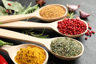 Photo of Different aromatic spices in spoons on black table, closeup