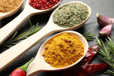 Photo of Different aromatic spices in spoons on black table, closeup