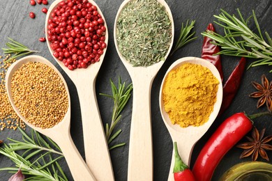 Photo of Different aromatic spices in spoons on black table, flat lay