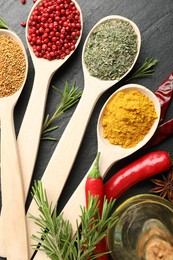 Photo of Different aromatic spices in spoons on black table, flat lay