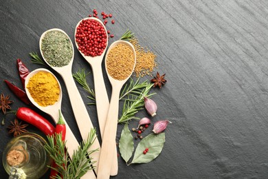 Photo of Different aromatic spices in spoons on black table, flat lay. Space for text