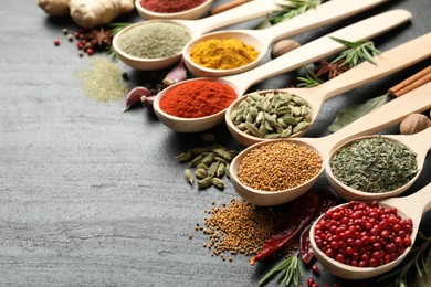 Photo of Different aromatic spices in spoons on black table, closeup. Space for text