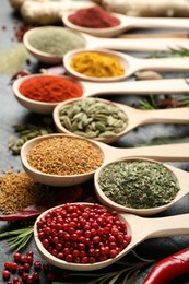 Photo of Different aromatic spices in spoons on black table, closeup