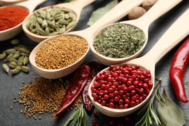 Photo of Different aromatic spices in spoons on black table, closeup