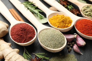 Photo of Different aromatic spices in spoons on black table, closeup