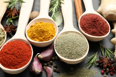 Photo of Different aromatic spices in spoons on black table, closeup
