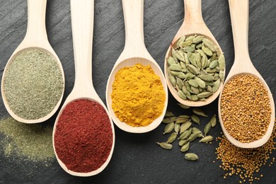 Photo of Different aromatic spices in spoons on black table, flat lay