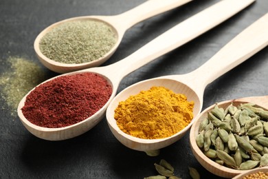 Photo of Different aromatic spices in spoons on black table, closeup