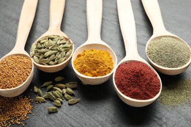 Photo of Different aromatic spices in spoons on black table, closeup