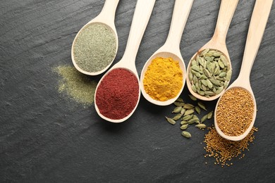 Photo of Different aromatic spices in spoons on black table, flat lay