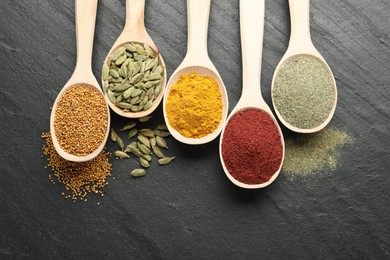 Photo of Different aromatic spices in spoons on black table, flat lay