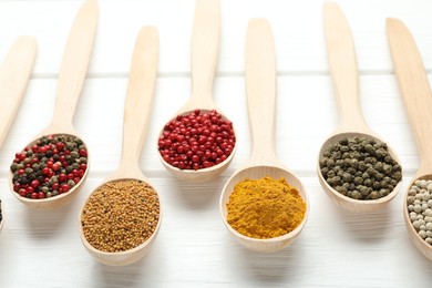 Photo of Different aromatic spices in spoons on white wooden table, closeup